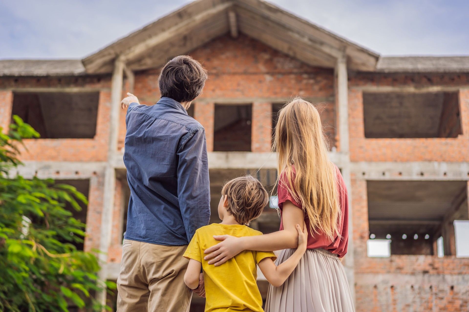 Family mother, father and son looking at their new house under construction, planning future and dreaming. Young family dreaming about a new home. Real estate concept